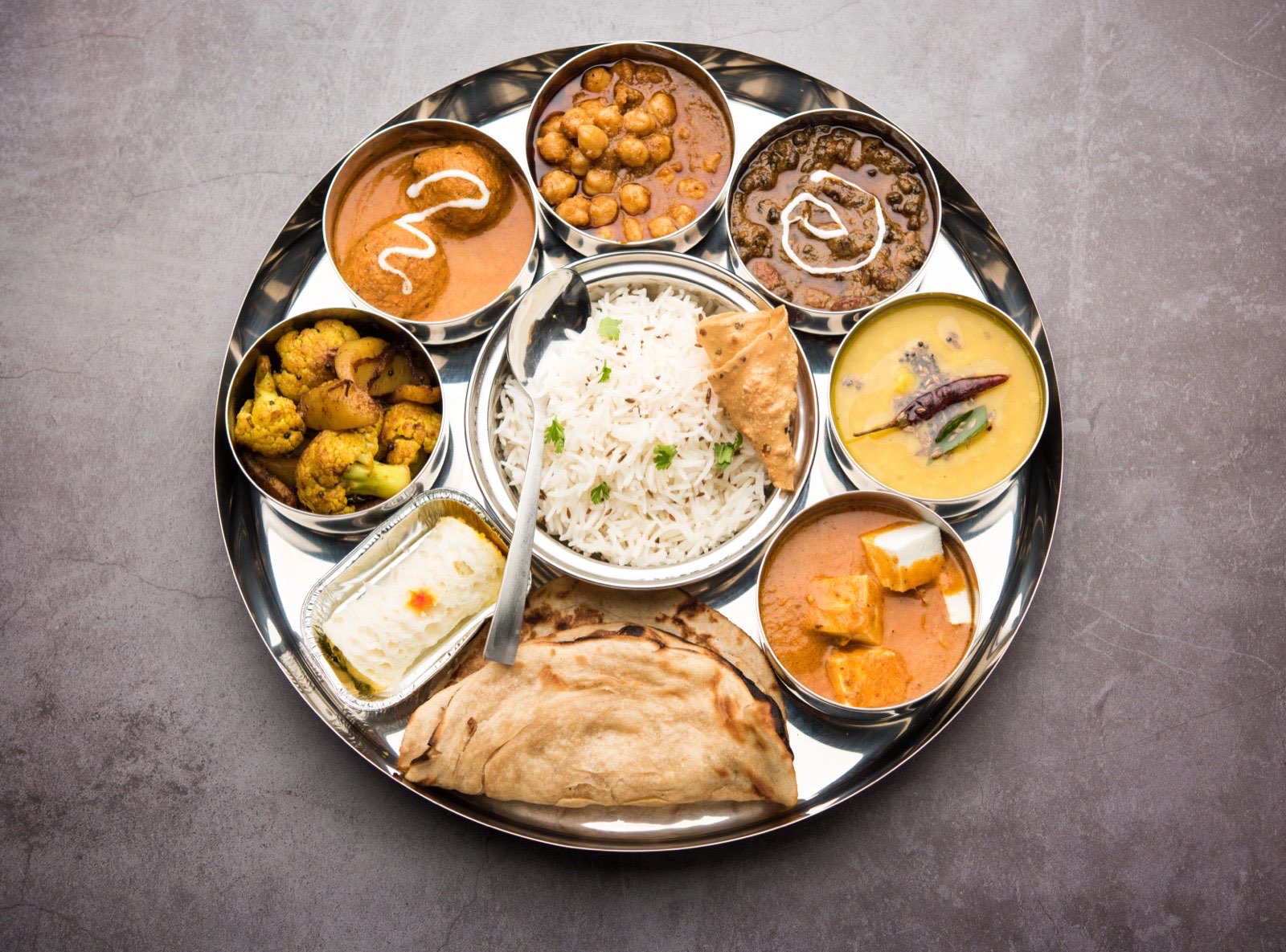 A vegetarian thali of ten small dishes around rice and breads